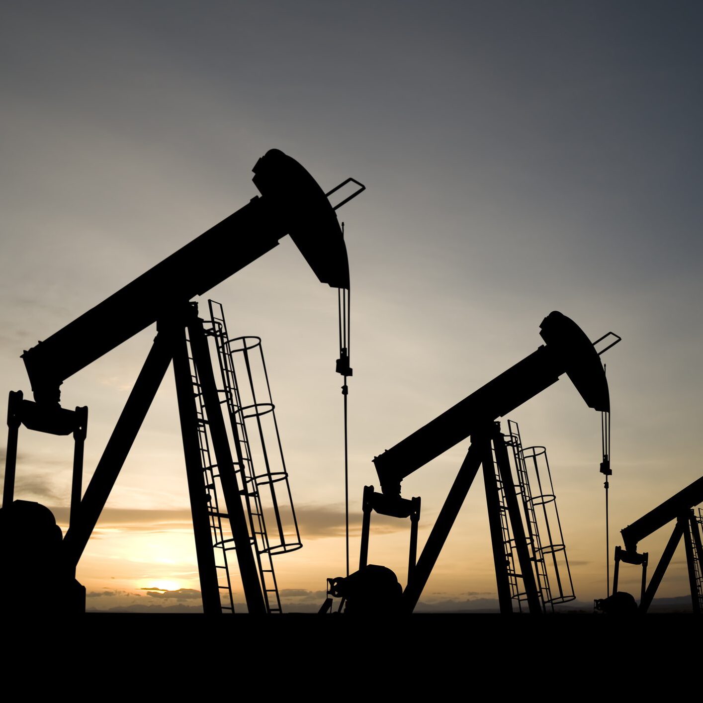 A royalty free image from the oil industry of three pumpjacks on a prairie at sunrise.